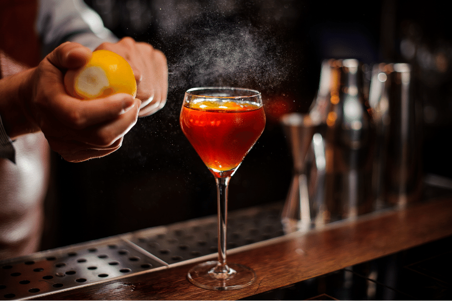 bartender adding a lemon garnish to a billionaire cocktail on bartop
